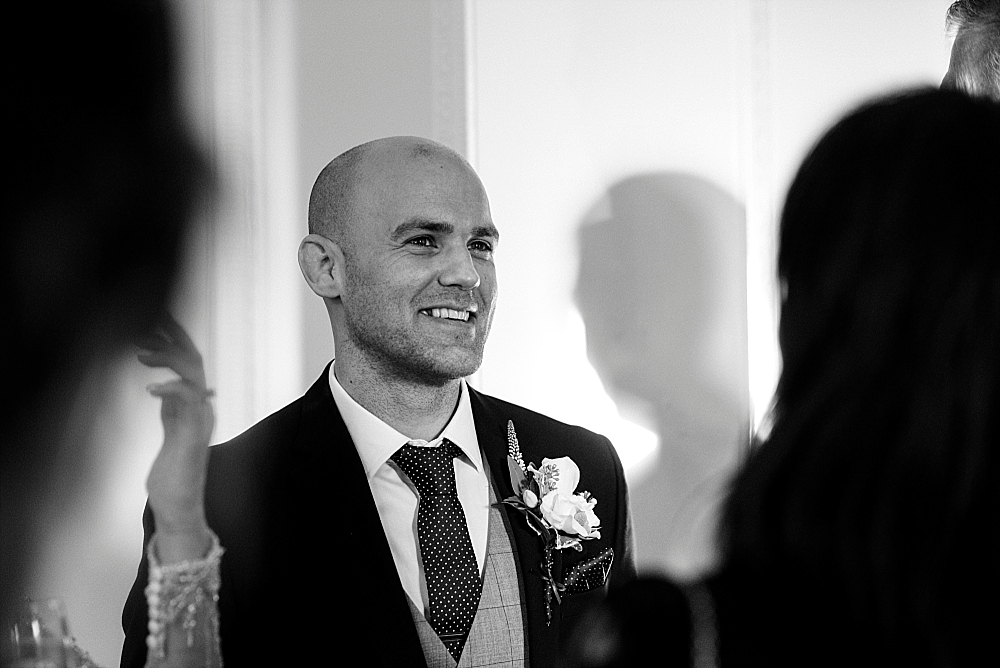 black and white photo of groom smiling in a crowd