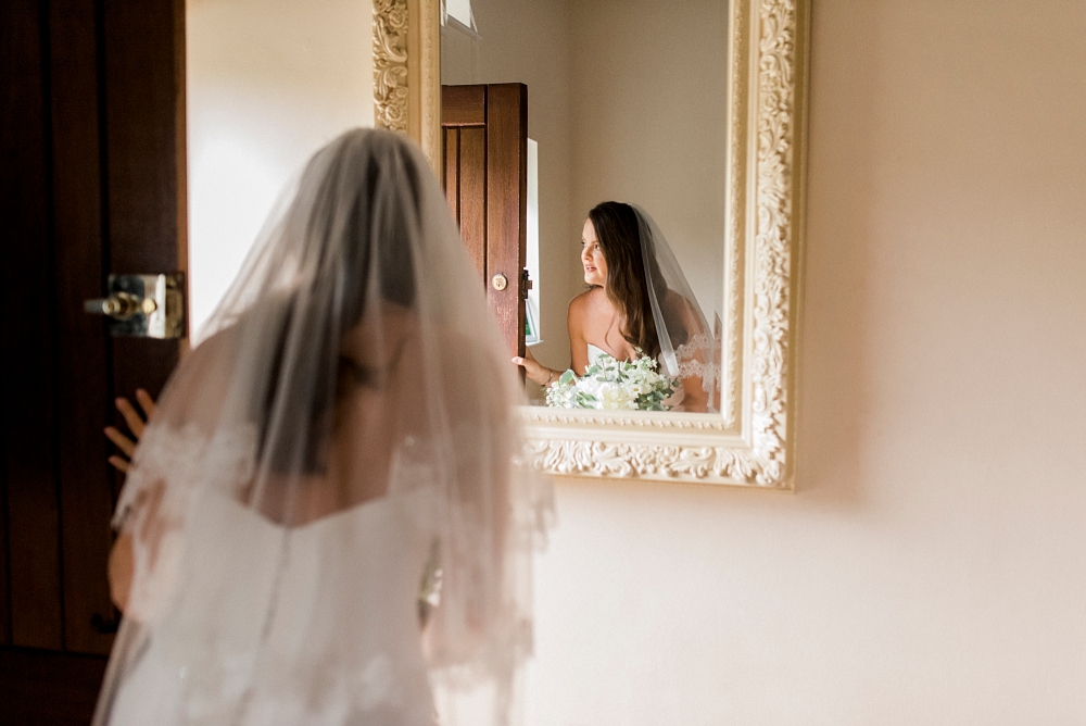bride ready to leave peepes out of front door with reflection in mirror