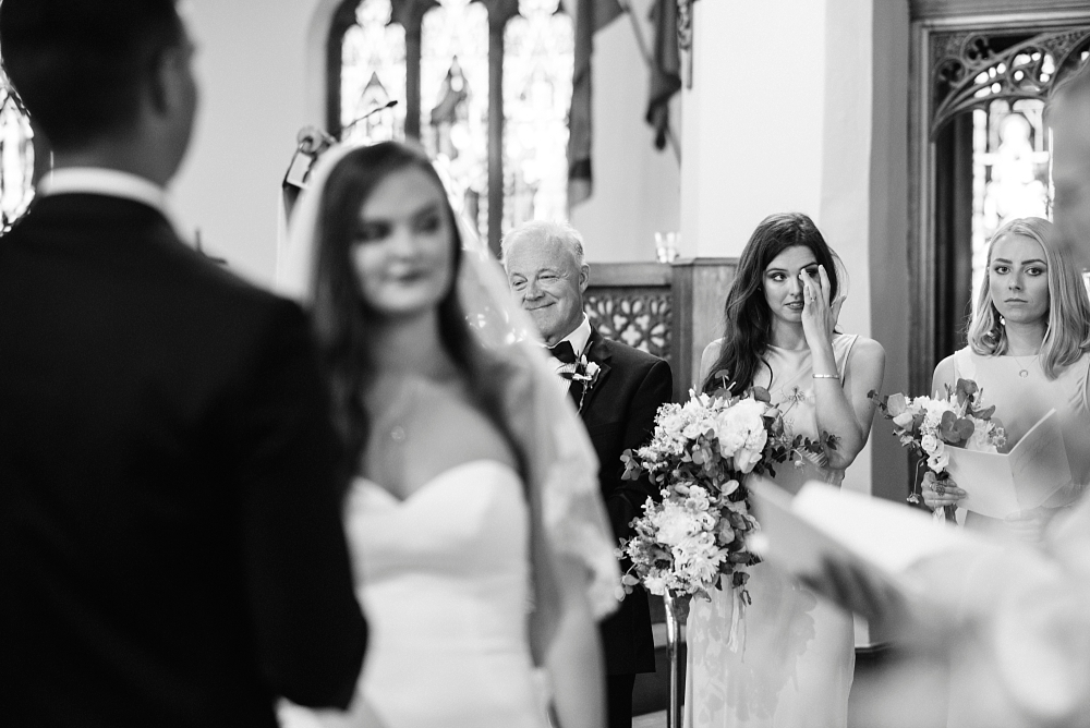 bridesmaid wiping away tear watching sister get married