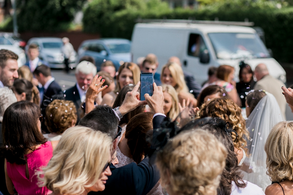 guest taking a photo with phone amongst wedding crowd