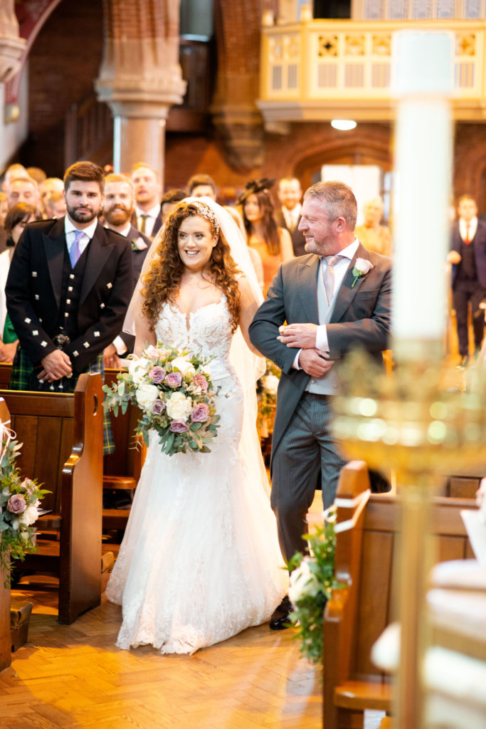 bride with ginger curly hair with her dad walking down the aisle at church