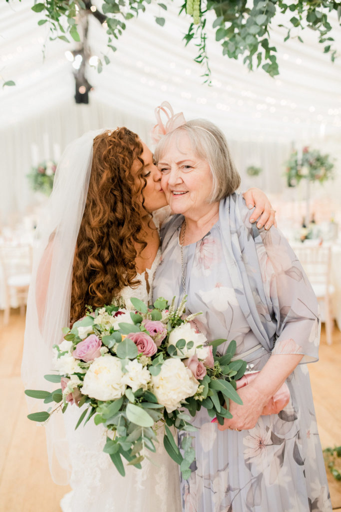 bride with long, curly, ginger hair kisses grandma on the cheek