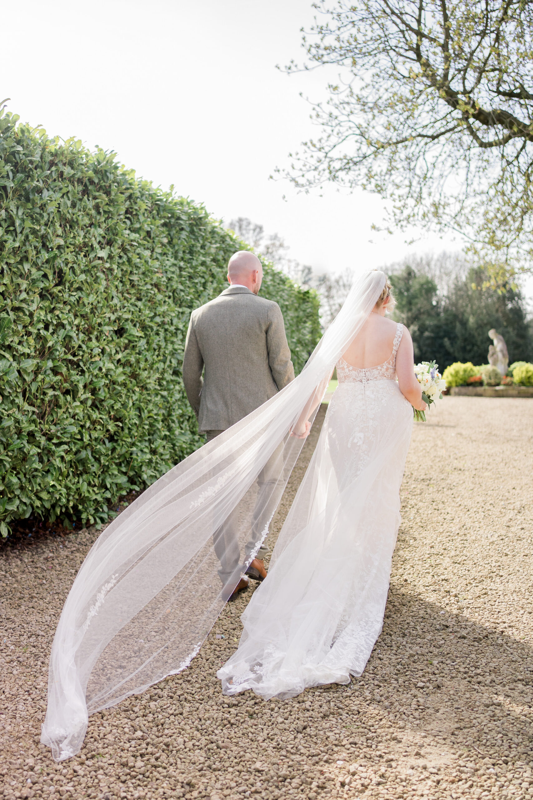 bride and groom walk on stone path with veil blowing in the wind