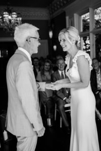 Black and white photograph of bride and groom exchanging rings at didsbury house hotel wedding ceremony