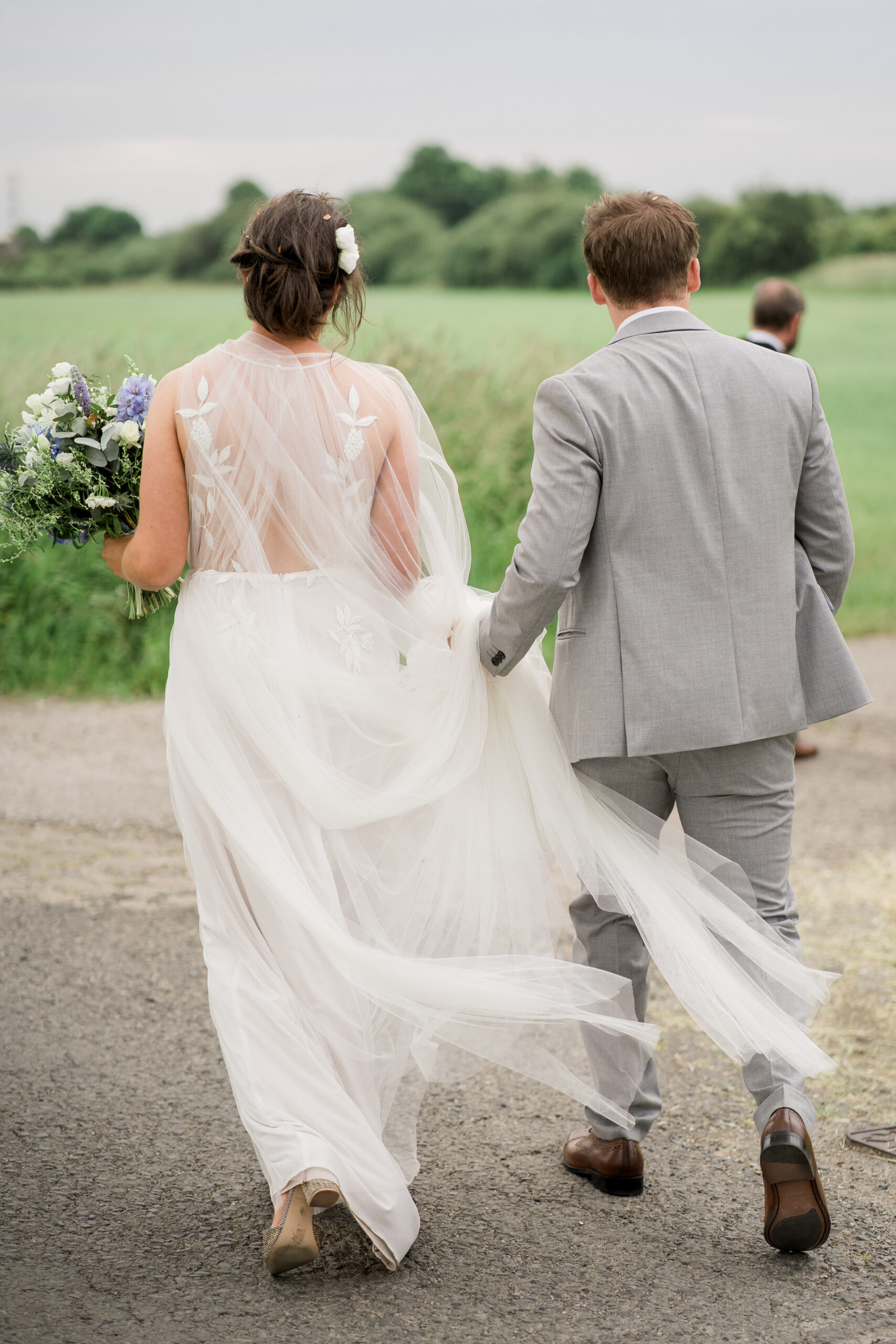 bride in white closet dress with cape, walking away from camera with groom