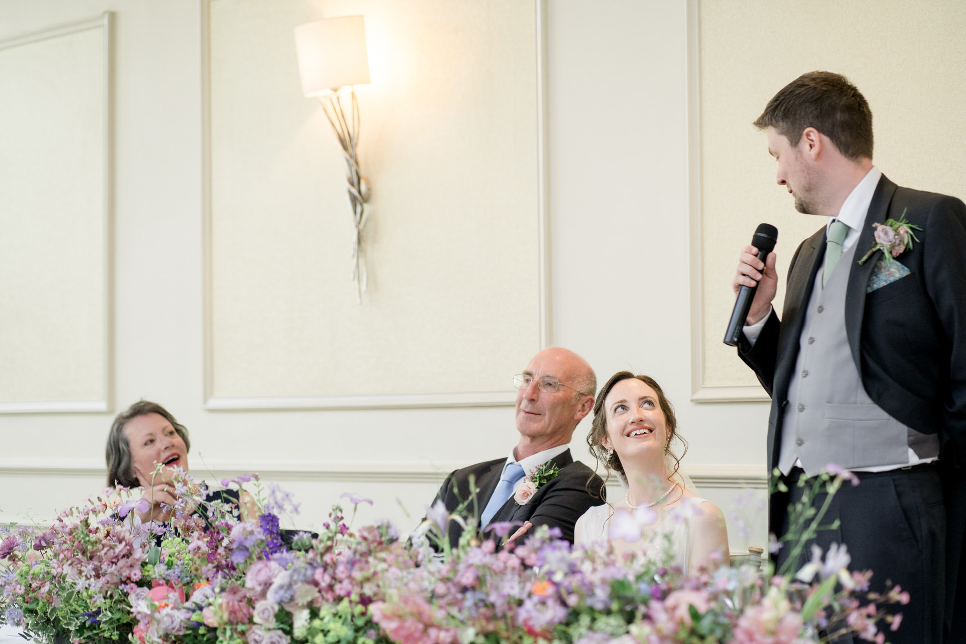 A Clifton Arms wedding with bright flowers. The groom gives his speech as the bride looks on.