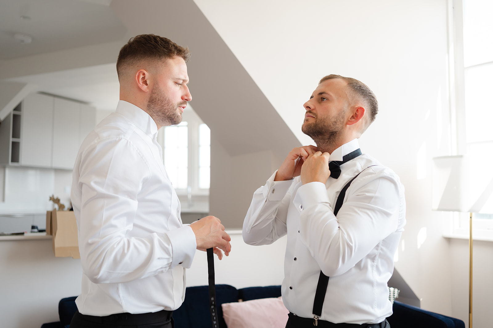 groom and best man putting black bow ties on