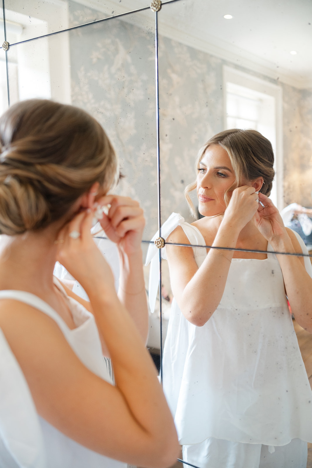bride in pyjamas adjusts earrings in the mirror at fourfold Hall dressing room