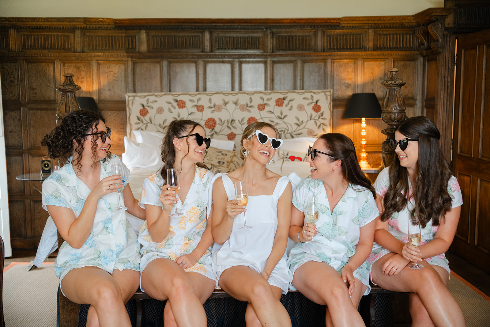 bride and bridesmaids sitting on the bed laughing with heart shaped sunglasses