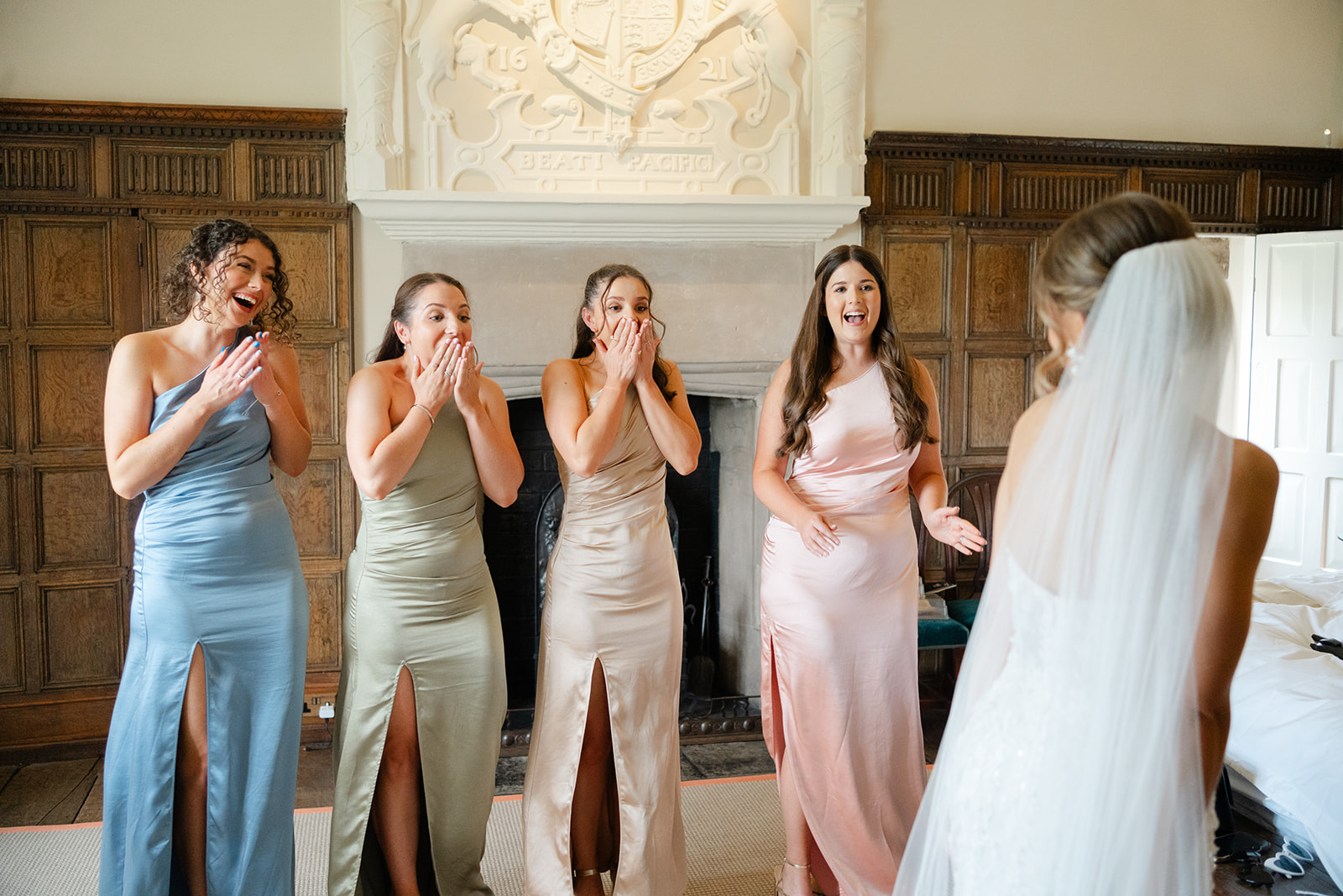 bridesmaids in pastel tutti frutti colours react to seeing the bride for the first time. With emotional faces and hands clasped over their mouths.