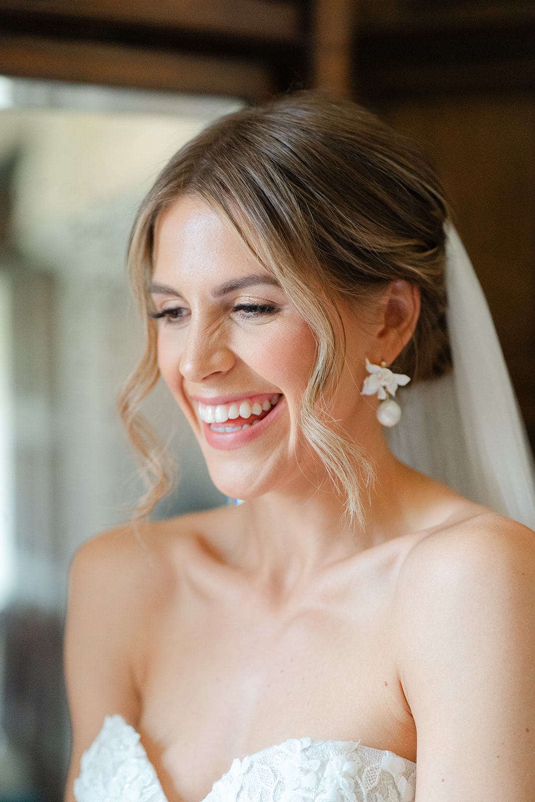 close up of smiley bride with hair up and soft curls, wearing oversized and pretty, white earrings