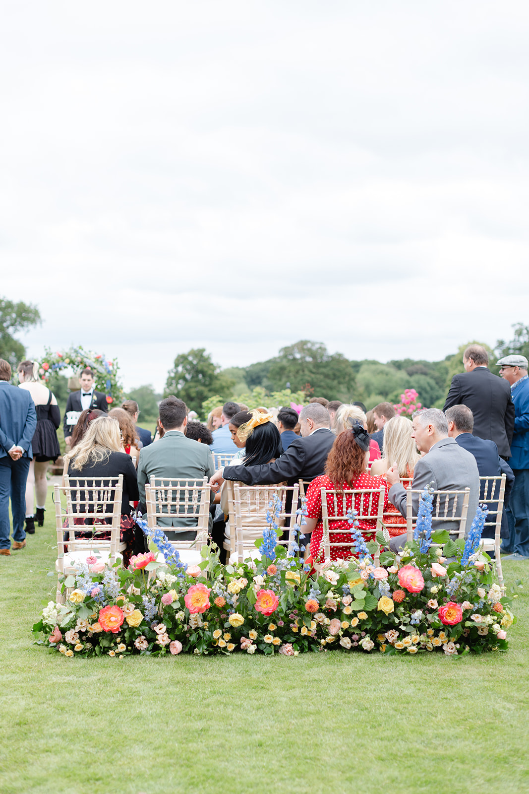 the back row of guests sitting in the ceremony setting, shot from behind to show flowers