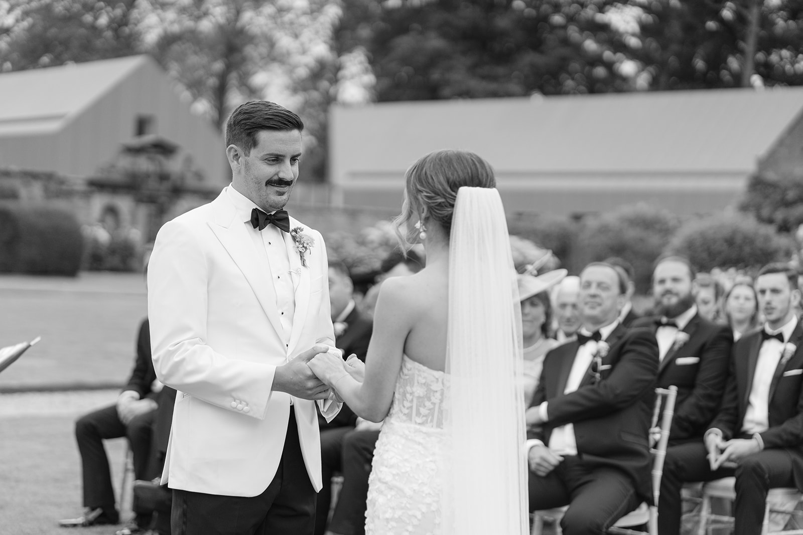 black and white photo showing the groom as his bride says her vows