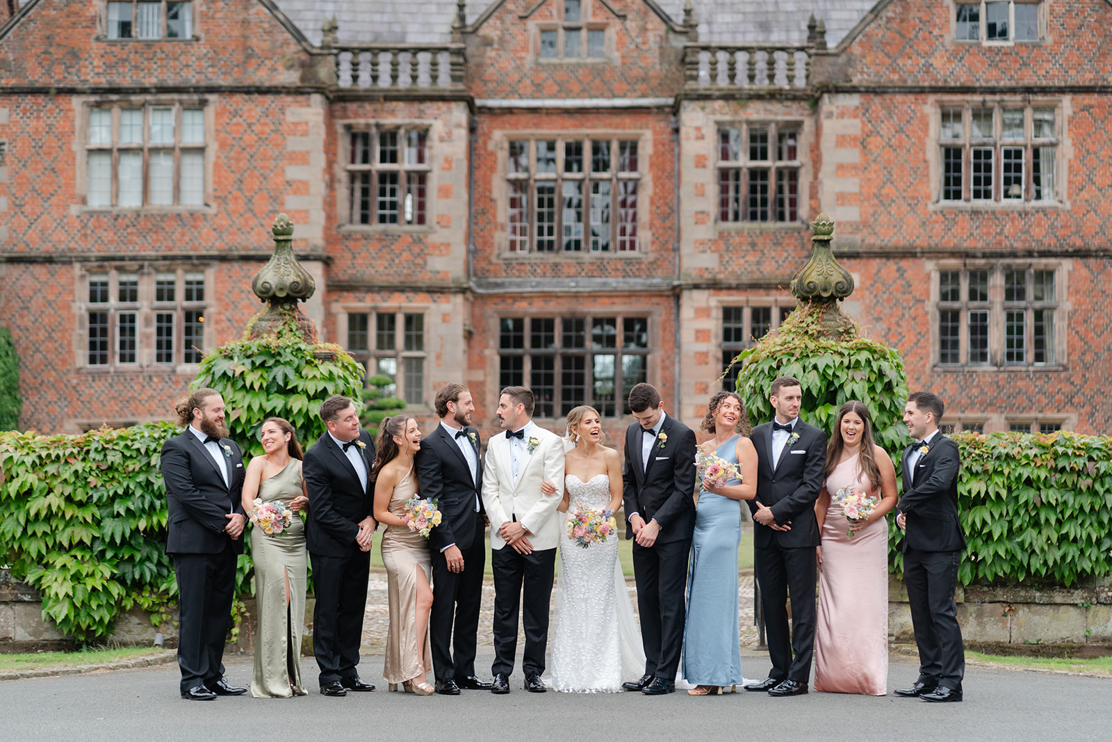 bride, groom and bridal party stand in line giggling for photograph in front of the impressive Dorfold hall