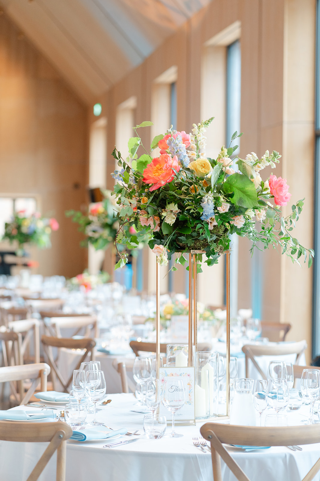 colourful flowers by the feel good florist sit on high pedestal in centre of a white clothed table at dorfold hall wedding