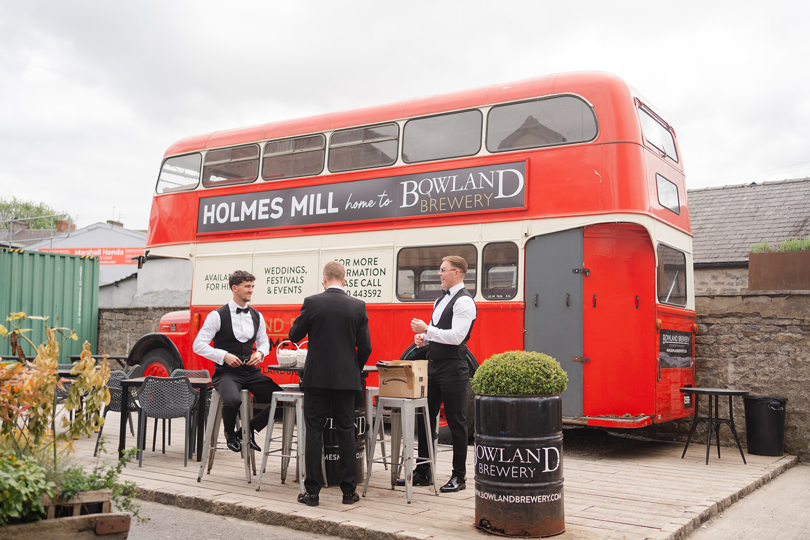 Groom and groomsmen gather at Holmes Mill Brewery in front of big red bus