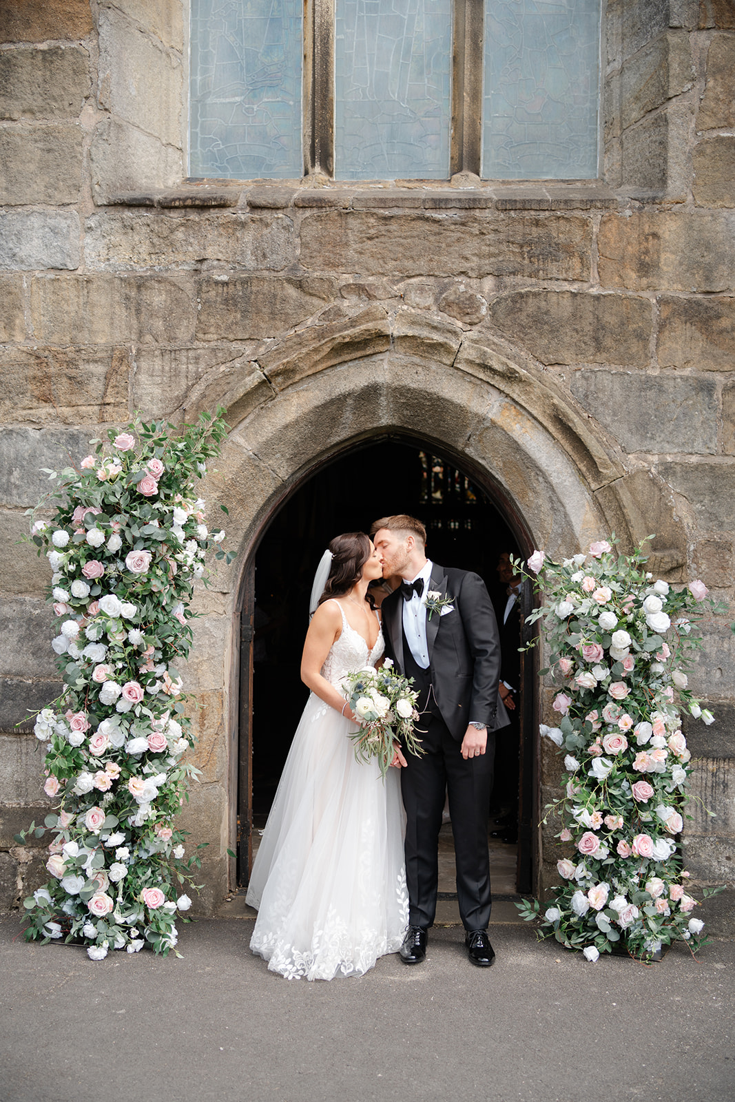 bride and groom exit Waddington church under flower arch