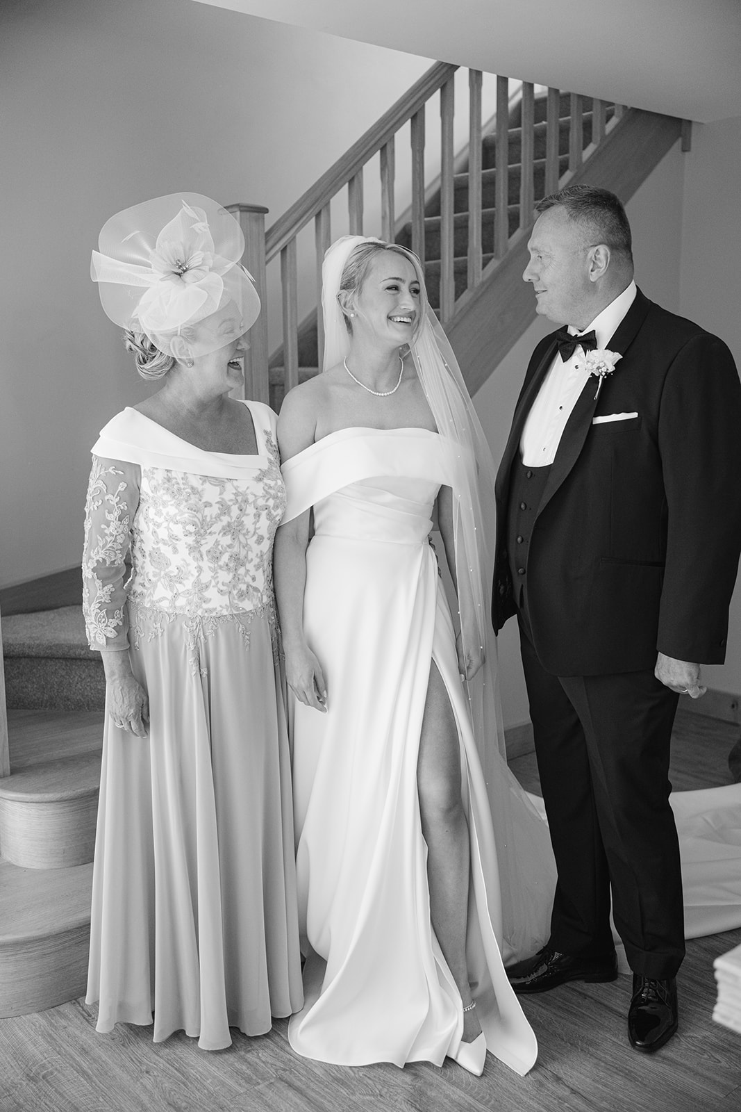 bride stands with mum and dad at bottom of staircase
