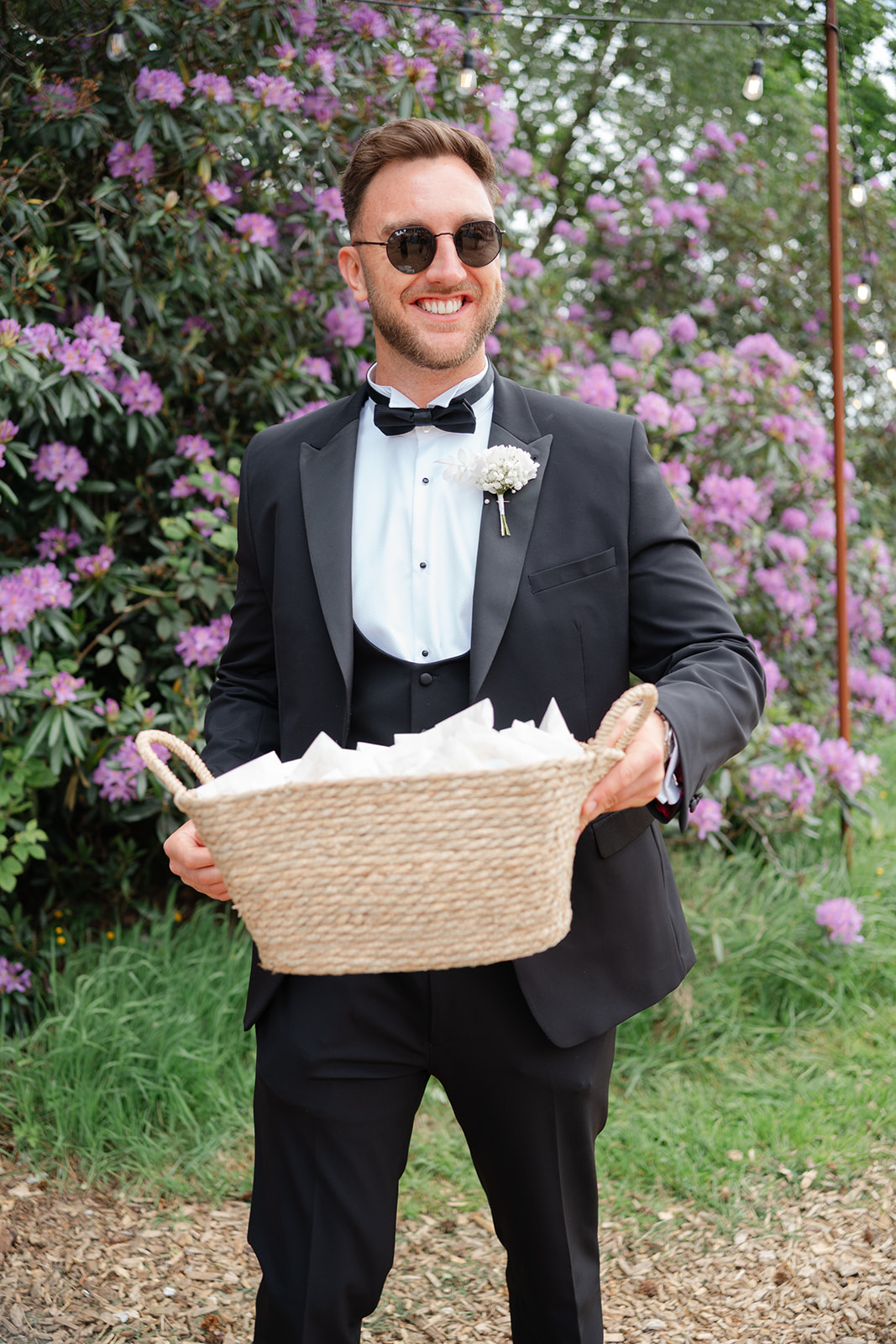 groomsman in black tie tux holding a basket full of confetti
